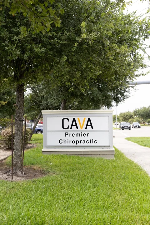 White roadside sign displaying CAVA and Premier Chiropractic beside the sidewalk on Broadway.